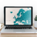 A map of Europe displayed on a laptop atop a desk with coffee cup and plant