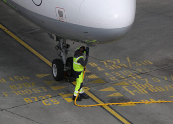 A ground crew worker connects a fuel hose to a jet