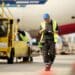 A man consults a tablet as he walks in front of a plane and ground support equipment