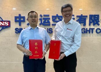 Two men holding red padfolios stand in front of a Sinotrans sign