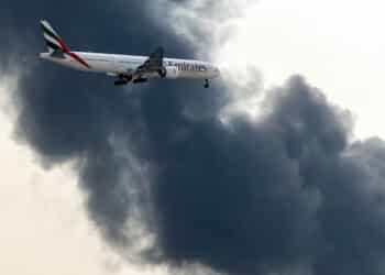 An Emirates aircraft prepares for landing as a smoke plume rises from an ongoing fire near Dubai International Airport on March 16. (Courtesy/Bloomberg)